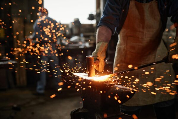 Close-up,Of,Blacksmith,In,Apron,Working,With,Hammer,And,Iron Schmieden und Hämmern als frühe Form des Metallverbindens
